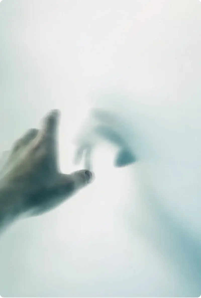 Two hands reaching toward each other through frosted glass, not quite touching.